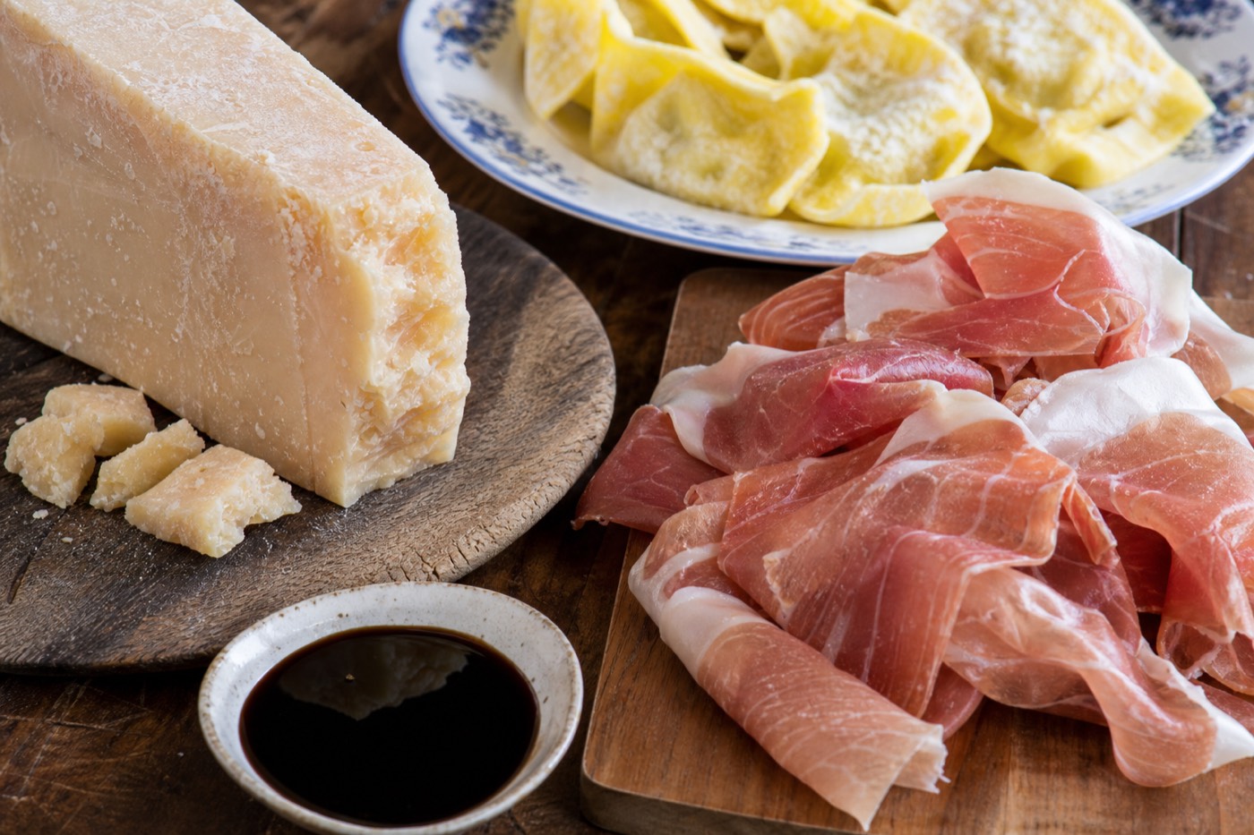 A wooden board with wedges of aged Parmigiano Reggiano and thin slices of Prosciutto di Parma, the two products Parma is best known for